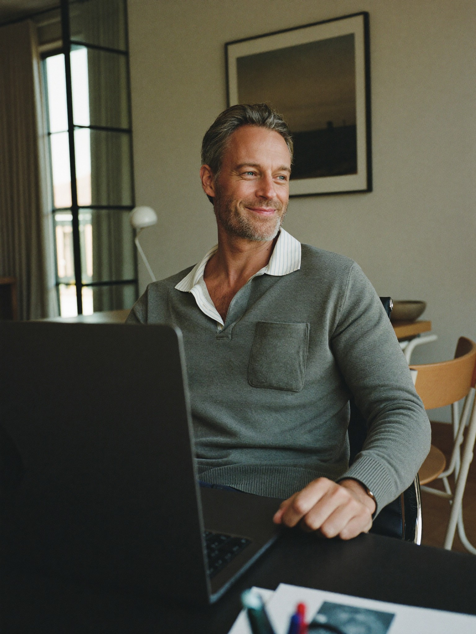 A relaxed, rested professional man in his early fifties at a home office in soft daylight, looking refreshed and composed